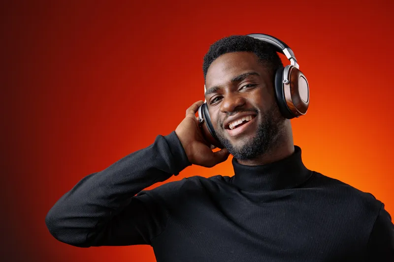 Smiling young Black man wearing headphones, enjoying music against a vibrant orange background, showcasing happiness and modern lifestyle