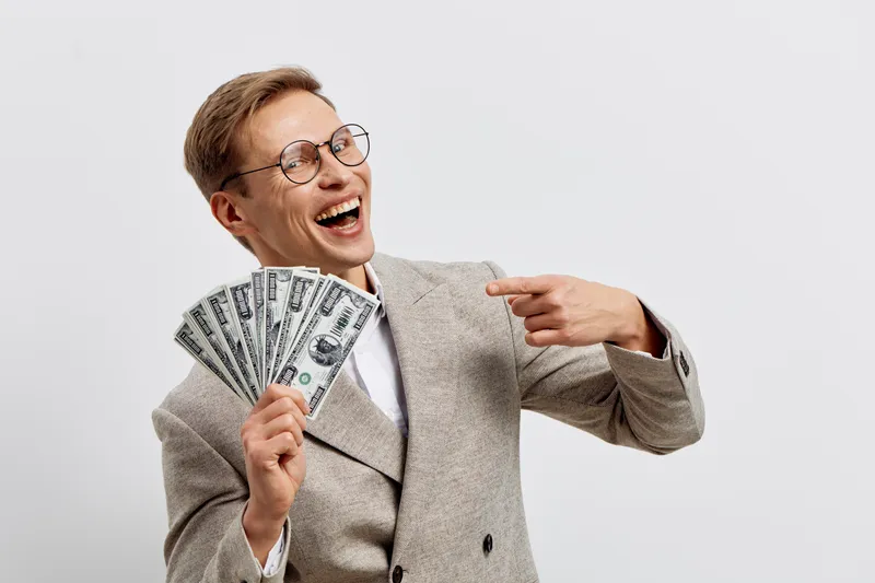 cheerful happy young caucasian man hold dollar cash money wear glasses beige coat studio portrait financial success concept
