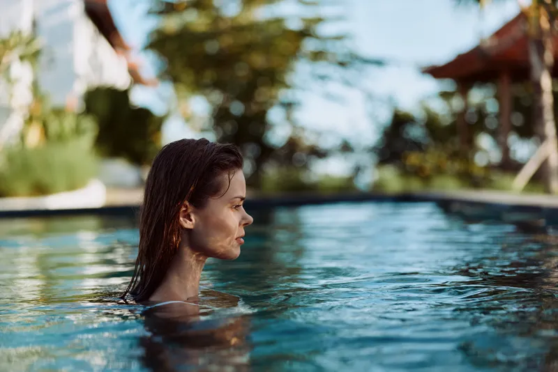 pool, woman, swimming, outdoors, relaxation A woman in a pool, seen in profile, enjoys a peaceful moment above shimmering water under bright sunlight. A lifestyle scene capturing relaxation and