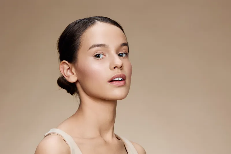 Elegant young woman with a natural look and minimal makeup, showcasing healthy beauty against a neutral background Youthful, serene expression and simple attire