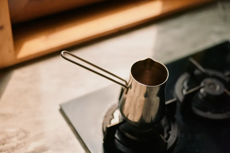 Coffee moka pot on a stove in a warm kitchen, metal surface gleaming as steam rises, capturing a cozy espresso ritual and everyday kitchen moment