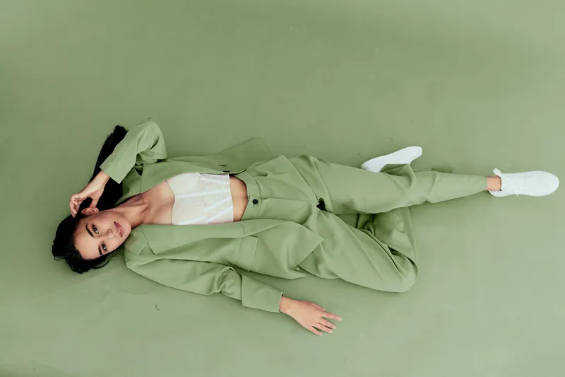 woman lying on green floor wearing light green suit and white sneakers, relaxed pose with hand near head, minimalist fashion style, soft lighting and monochrome background
