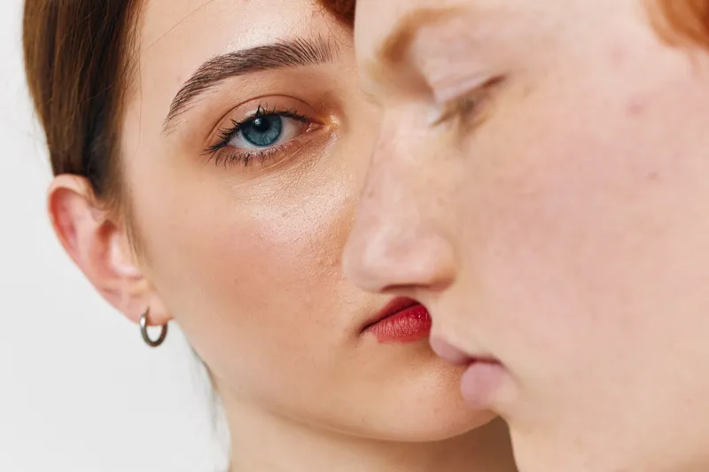 Closeup of two young women faces with serious expression, natural skin texture, minimal makeup, and neutral background for beauty and friendship concept.