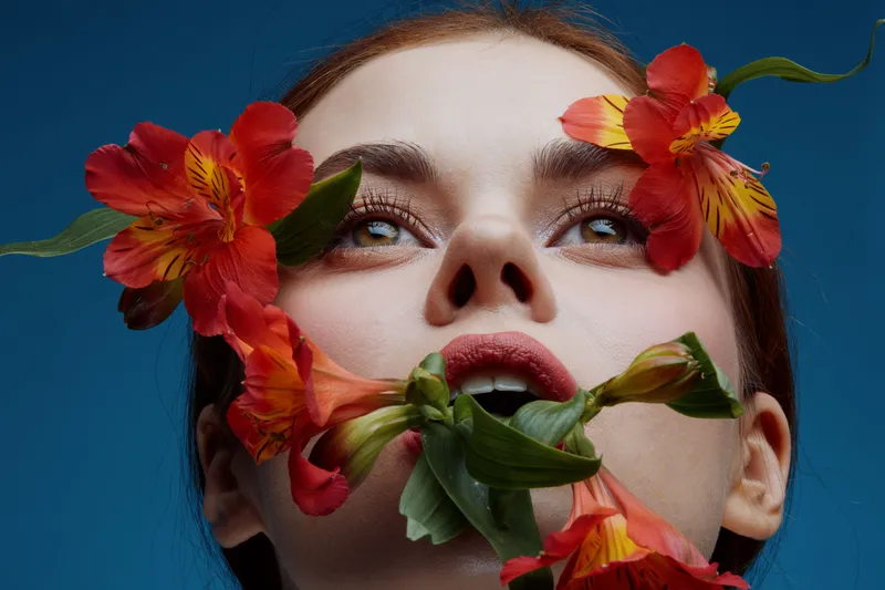 A serene portrait of a young woman with vibrant flowers, showcasing beauty and nature with a lively blue background, ideal for concepts related to wellness and floral art