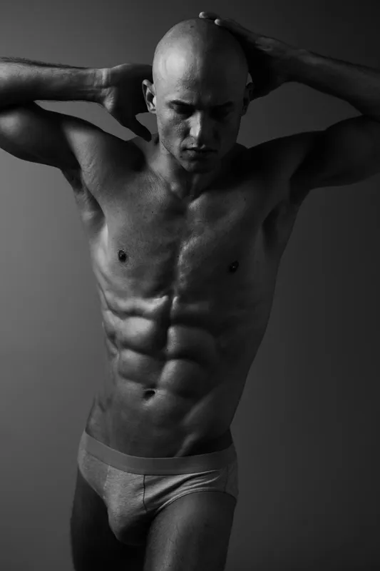 Black and white image of a muscular man posing confidently, showcasing strength and fitness in a dynamic composition.