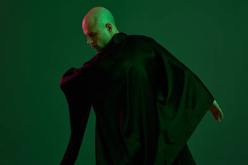 A man in a flowing dark robe showcases elegance against a vibrant green backdrop, capturing a striking black and white aesthetic in a bold artistic expression.