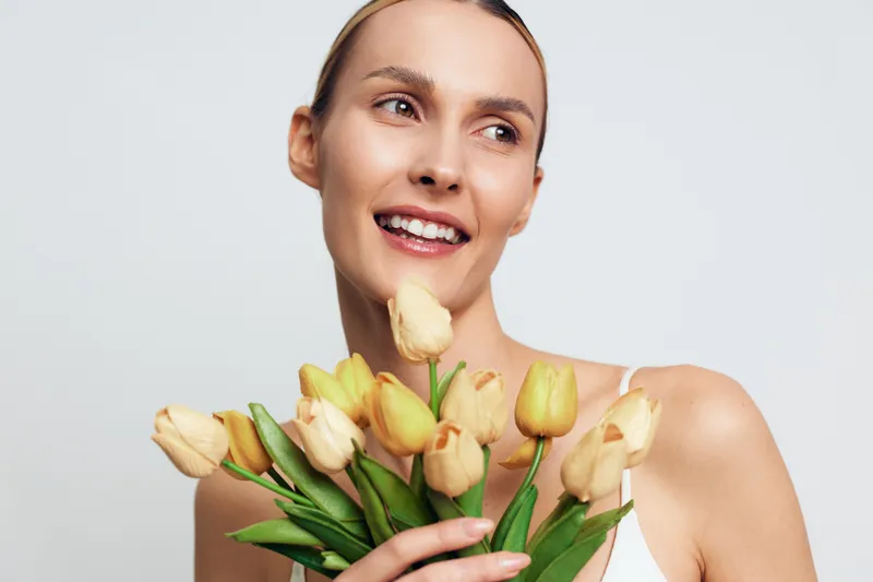 Woman portrait holding tulips bouquet, smiling in studio light, fresh flowers for spring, elegant beauty and skincare concept, soft focus, clean white background, joyful mood and relaxation