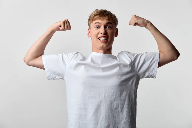 Energetic man flexing arms in a white tee, celebrating achievement with a bold, upbeat pose and confident mood in a clean studio setting with bright light