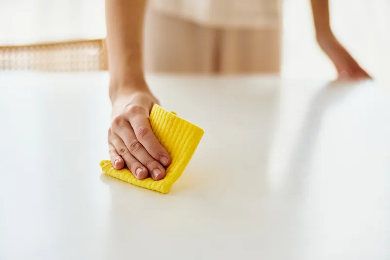 Cleaning hands wipe white table with yellow cloth, household surface cleaning and tidy home. Closeup of person wiping kitchen or dining table for hygiene and neatness.