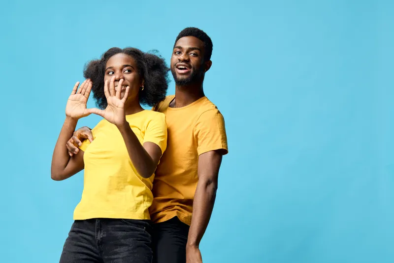 Cheerful African American couple in matching yellow t shirts posing against a blue background, expressing joy and love