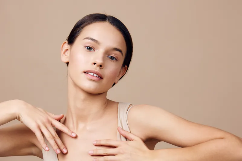 Natural beauty portrait of a young female model with neutral makeup, soft skin, and a confident expression against a beige background
