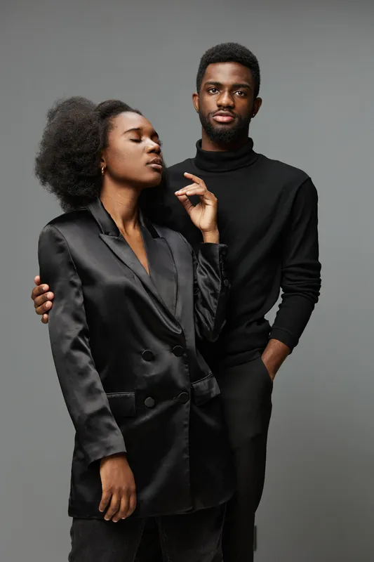 Stylish couple in elegant black attire posing confidently against a neutral backdrop, showcasing modern fashion and strong emotions in a contemporary style
