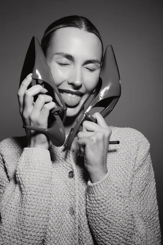Happy caucasian woman with light skin holding shiny high heel shoes near face with eyes closed and tongue out. Concept for fashion, fun, and lifestyle with joyful female model.