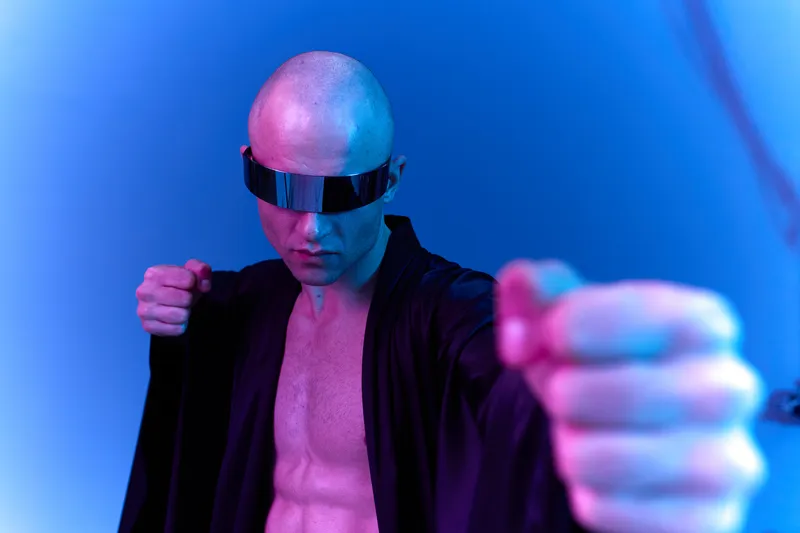 Strong man with sunglasses showing determination, dressed in a black robe, set against a vibrant blue background. The image conveys a futuristic and bold vibe.
