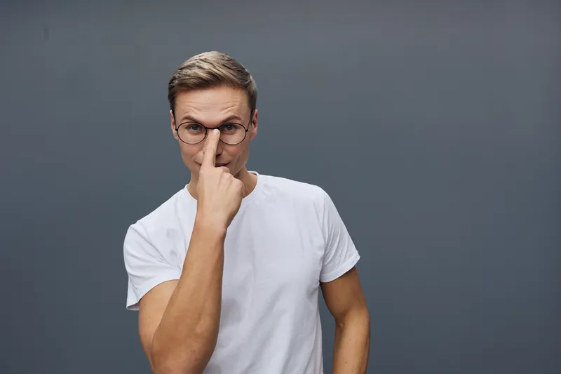 Young man wearing eyeglasses casual white t-shirt touch nose look camera confident smart home technology concept