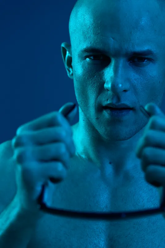 Confident man in blue light, showcasing strength and determination with a focused expression and a distinct look. This black and white image captures intensity and emotion.