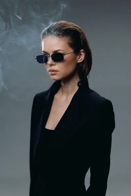 Stylish woman wearing black sunglasses and a sleek black outfit with neutral background and moody lighting