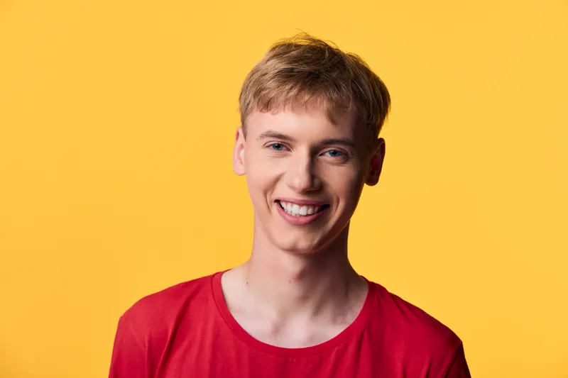 Smiling man in a red shirt against a vibrant yellow background, conveying a happy expression and bright colors, ideal for casual style lifestyle and advertising campaigns