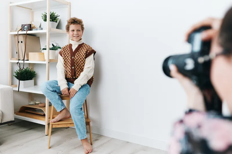 An authentic portrayal of a student at play, posing in a home studio with a knitted vest, suggesting genuine school life and candid lifestyle imagery.