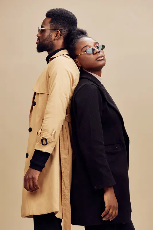 Stylish couple wearing contemporary fashion, with the man in a beige trench coat and the woman in a black blazer, showcasing modern urban elegance and confidence
