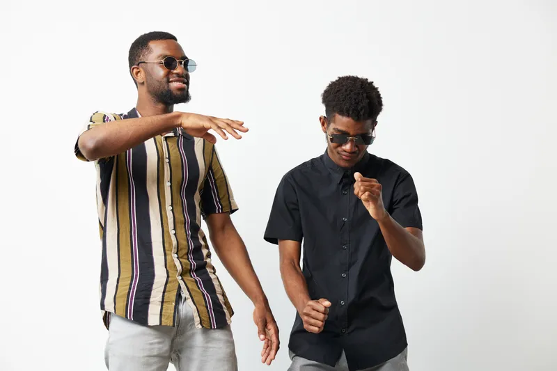 Joyful African American men dancing together, showcasing happiness and friendship in a modern setting. Their stylish outfits enhance the vibrant atmosphere of the moment.