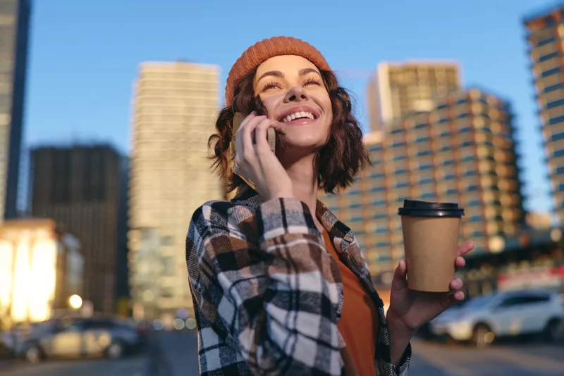 woman coffee phone city smile beanie candid golden portrait of a young woman talking on phone with coffee in hand, candid lifestyle, authenticity and golden hour glow with emotional storytelling.