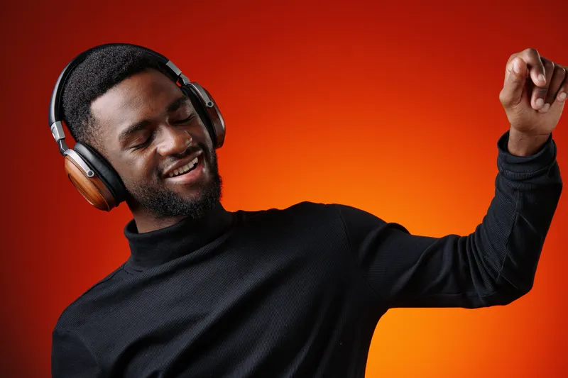 Happy young Black man enjoying music with headphones on an orange background, expressing joy and relaxation in a modern and vibrant setting