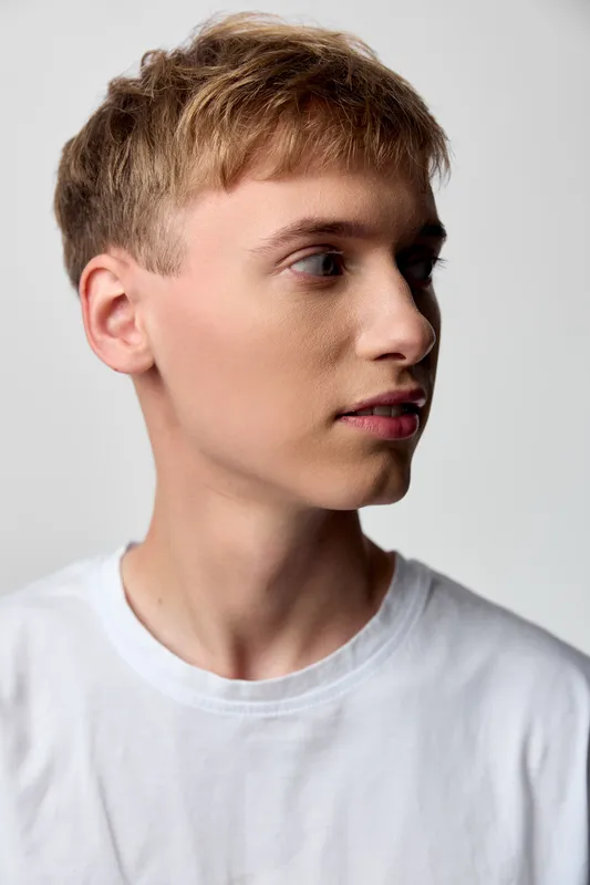 Young man profile with blond hair, short hair, white t shirt, studio lighting, neutral background, calm expression and minimalist styling for stock photography and modern branding