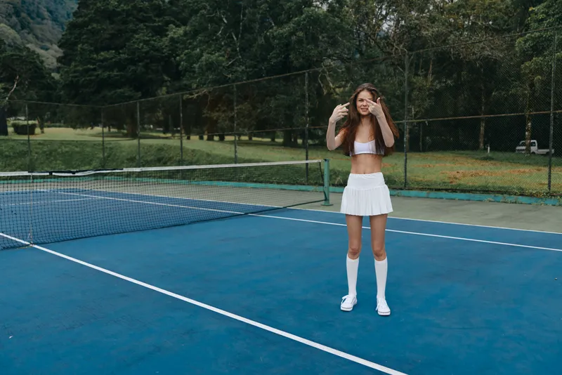 Young female athlete celebrating a successful moment on the tennis court, wearing a white sports outfit, evoking joy and confidence in a lush green environment