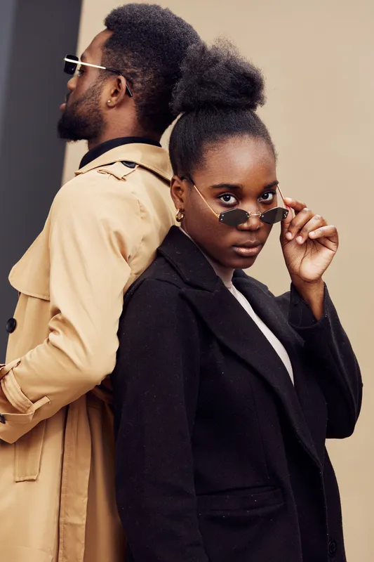Stylish black models in fashionable sunglasses pose back to back against a minimalistic backdrop, showcasing contemporary fashion and confidence in a neutral color palette