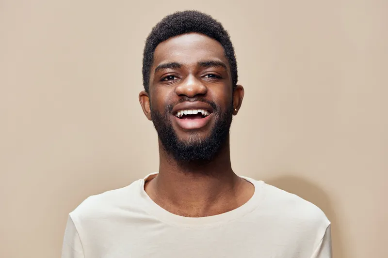 Happy young man smiling in a neutral toned shirt against a warm beige background, representing positivity and self confidence