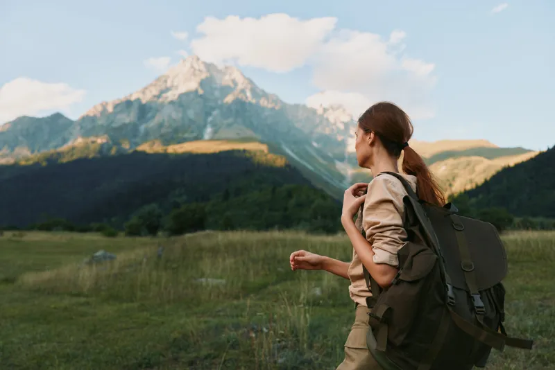 Woman hiking with backpack in a grassy meadow before distant mountains, embracing nature and outdoor lifestyle, peaceful landscape and travel vibe