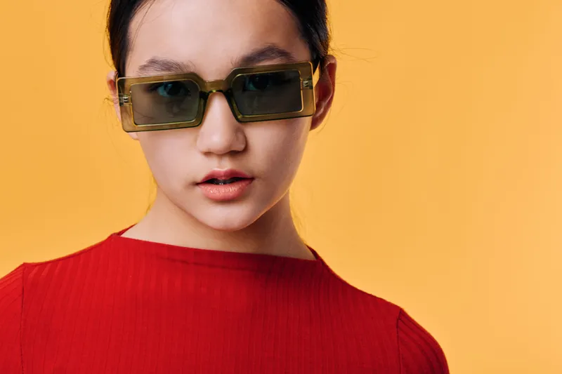 Woman with sunglasses and red shirt posing on yellow background for fashion portrait and style concept with confident expression and modern look at studio shoot.