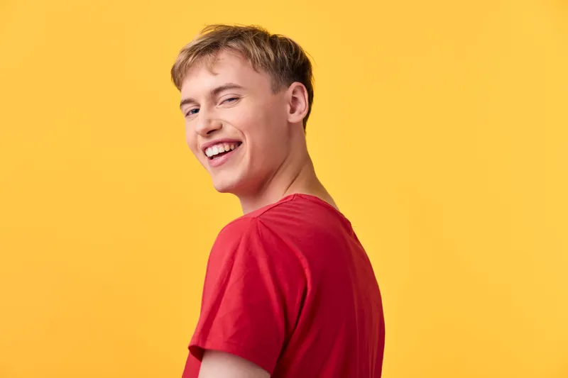 Smiling man in a red shirt stands against a vibrant yellow backdrop, conveying casual energy and upbeat mood suitable for lifestyle, fashion, and smile themed campaigns.