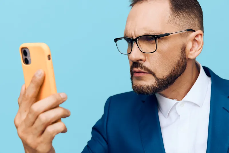 A professional businessman focused on his smartphone, isolated against a solid blue background. The colored backdrop emphasizes determination, focus, and calm confidence in a modern work moment.