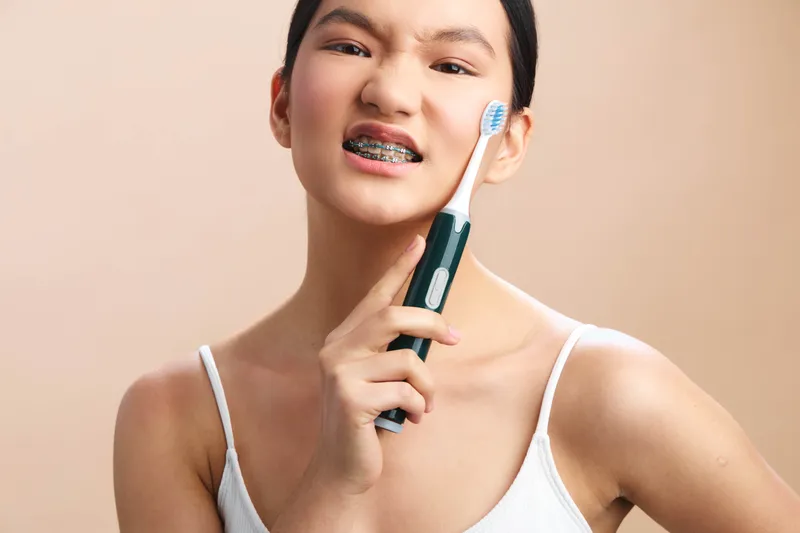 Asian woman brushes her teeth with an electric toothbrush in a modern bathroom, smiling confidently as she starts a fresh daily routine for health and confidence in calm clean space with soft light