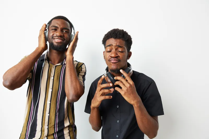 Happy African American men enjoying music together, expressing joy and excitement while listening through headphones. Captivating energy and connection are evident.