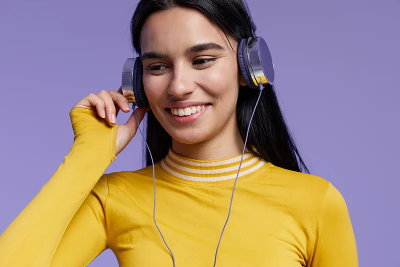 Young woman sport fitness enthusiast wearing headphones and a yellow top, smiling and enjoying music during workout or relaxation with a calm purple background.