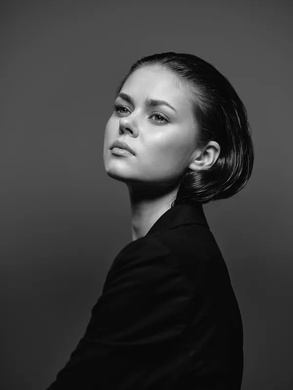 Black and white portrait of a pensive woman with short hair wearing a dark outfit in studio lighting.