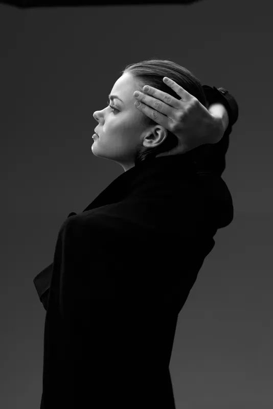 Black and white portrait of a thoughtful woman in a dark coat with braided hair against a gradient background.