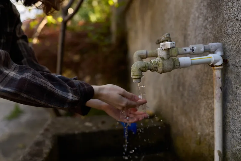 A closeup of a woman washing hands under an outdoor faucet in natural light, capturing a simple daily routine, selfcare, and hygiene in a casual outdoor setting