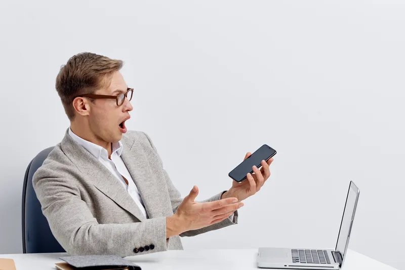 surprised man with glasses hold smartphone look shocked digital nomad remote work technology concept modern workspace white background