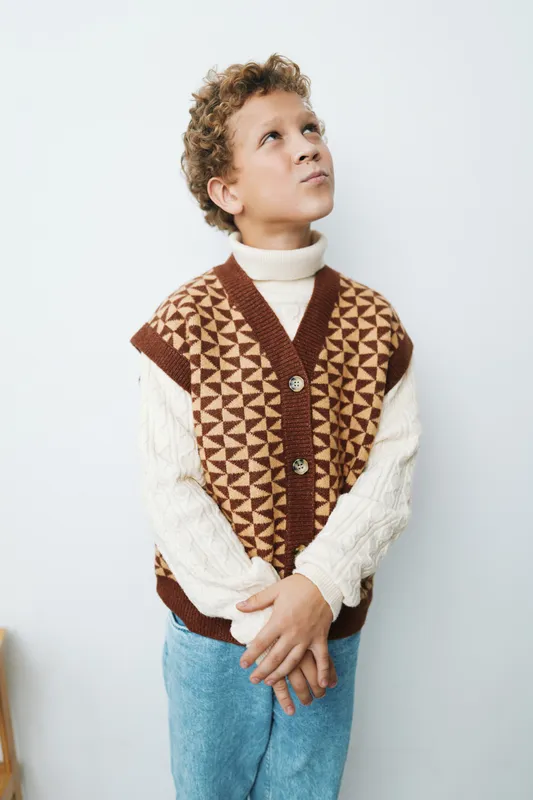 Authentic student style captured in a thoughtful moment, a child wearing a patterned knit vest and turtleneck, embodying curiosity, play, and everyday school life.