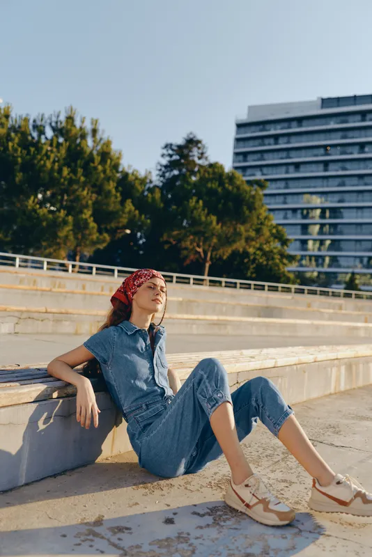 Lifestyle woman in modern boho-western denim street style with red bandana, relaxed pose outdoors, film color effect capturing casual summer mood.