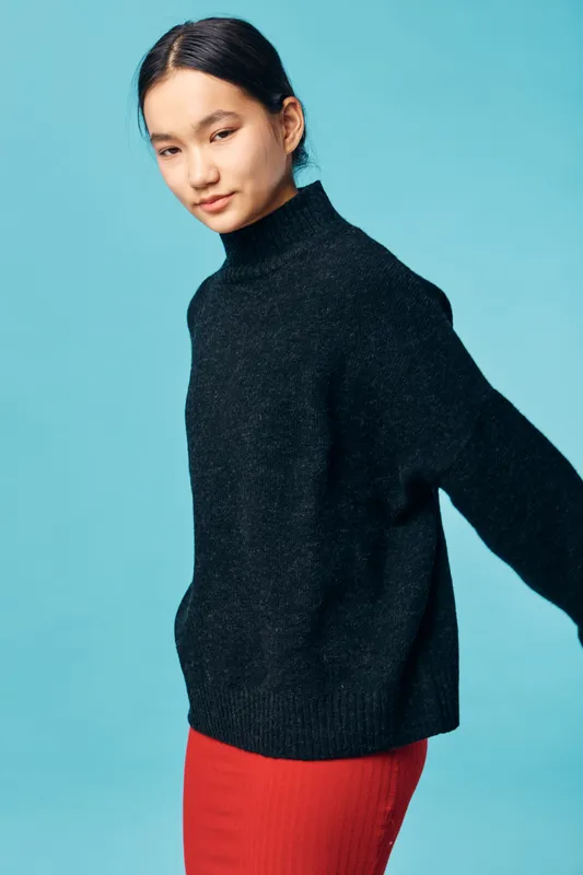 Young woman in black knitted sweater and red skirt posing with eyes closed against blue background. Casual fashion, relaxed posture and simple studio portrait of female model.