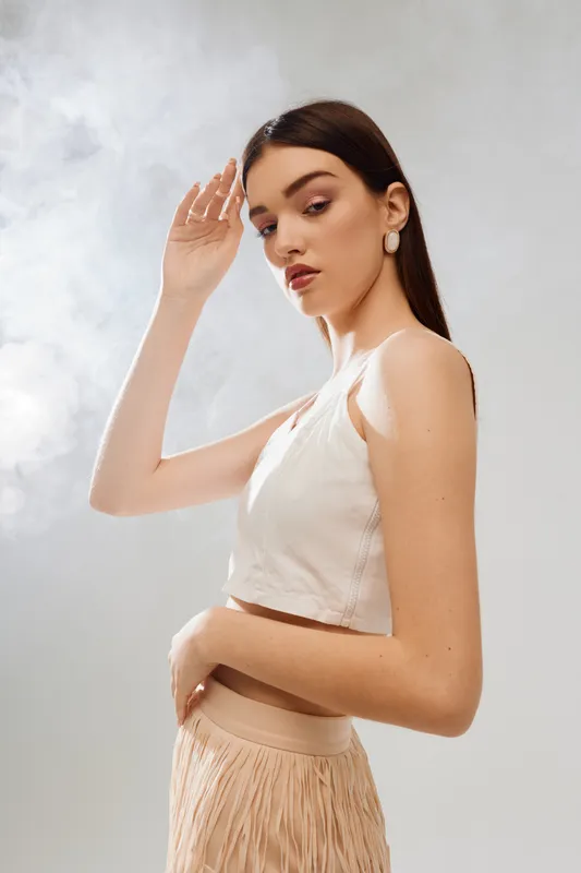 Young woman beauty fashion model poses with hand near face wearing white top and beige skirt. Studio shot on light background. Concept for style, elegance, and modern trends.