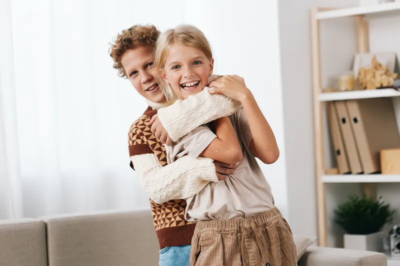 A joyful scene of an adult embracing a smiling child indoors, capturing warmth, connection, and a candid, affectionate moment in a bright living room setting.