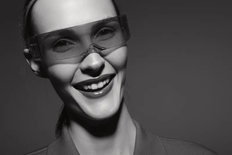 Smiling young white woman wearing protective glasses against grey background. Studio portrait with soft lighting and natural beauty, concept of safety and confidence.