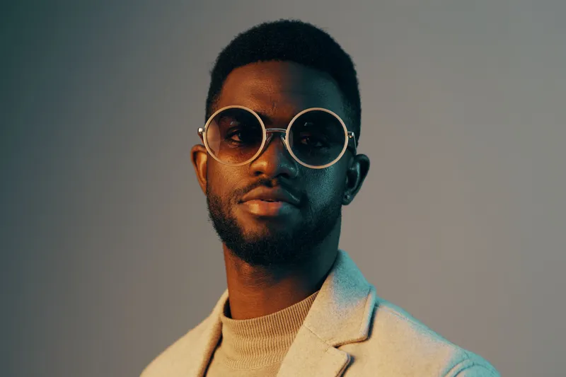 Stylish African man in modern eyewear, wearing a fashionable gray blazer and turtleneck, exuding confidence and sophistication against a gradient background