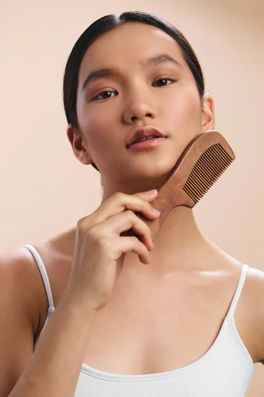Asian woman is shown in a close up portrait as she gently combs her hair with a wooden brush, creating a calm beauty moment in soft lighting.